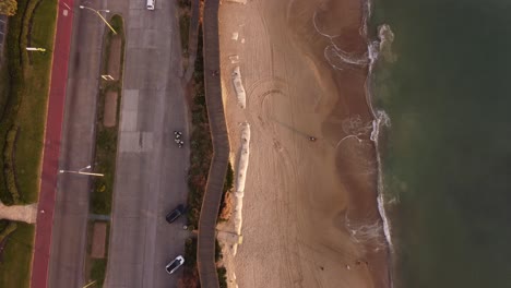 Aerial-top-down-shot-of-sandy-beach,-ocean-and-cars-on-road-in-Punta-del-Este,Uruguay