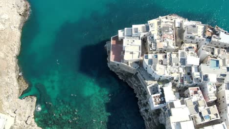 Drone-capture-high-altitude-shot-of-Polignano-a-Mare-a-town-in-Italy-with-numerous-building-constructed-on-the-edge-of-the-cliff-with-people-swimming-in-the-Adriatic-Sea