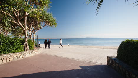 Noosa-Heads-Main-Beach-Boardwalk-With-Tourists-Walking-Beachside,-4K-Slow-Motion