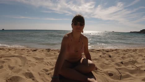 A-girl-sitting-on-sand-on-a-sunny-sandy-beach-in-Greece