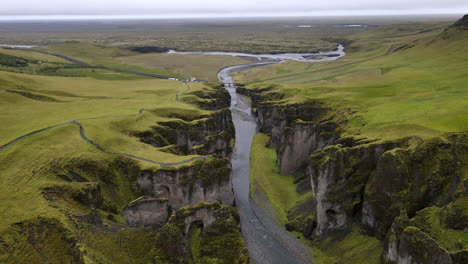 Aerial-shot-over-the-green-mountains-and-the-river-of-Fjadrargljufur-canyon,-in-Iceland