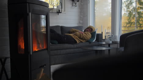 Man-lying-on-sofa-than-a-nap-in-a-warm-room-with-a-burning-stove