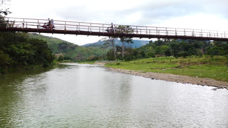 Motos-Conducen-En-Un-Puente-Peatonal-Sobre-Un-Río-Tranquilo-En-El-Parque-Nacional-Phuoc-Binhg,-Vietnam