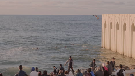 Wide-shot-of-young-man-diving-from-high-wall-into-Atlantic-Ocean-as-others-watch-on,-Casablanca-Morocco