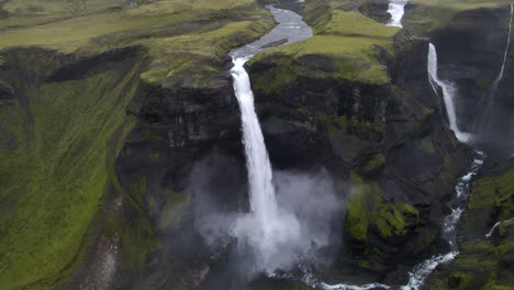 Aerial-circle-panning-tracking-shot-of-the-incredible-Haifoss-waterfall-in-the-mountain-gorge-of-Fossárdalur,-in-Iceland