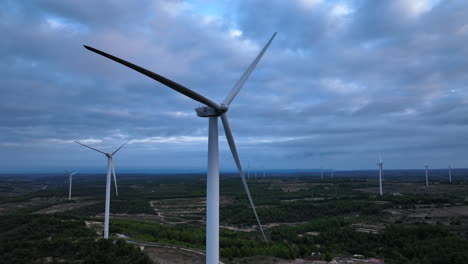 Aerial-view-flying-towards-stationary-renewable-wind-turbines-on-overcast-Barcelona-farmland