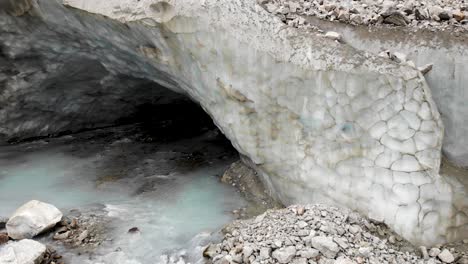 Aerial-flyover-from-the-ice-cave-of-the-Zinal-glacier-in-Valais,-Switzerland-with-a-view-of-the-melting-glacial-water-stream-and-crevasses