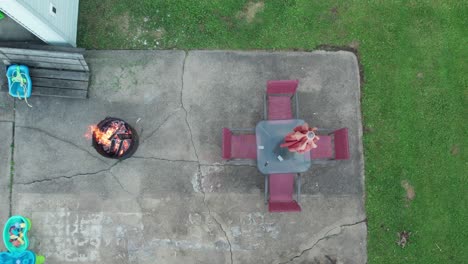 -Aerial-drone-bird's-eye-view-over-a-campfire-burning-in-a-garden-outside-a-house-at-daytime
