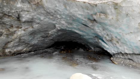 Aerial-flyover-from-the-ice-cave-of-the-Zinal-glacier-in-Valais,-Switzerland-with-a-view-of-the-melting-glacial-water-stream,-crevasse-and-alpine-valley