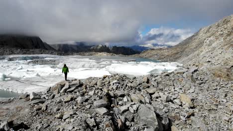 Sobrevuelo-Aéreo-Sobre-Un-Excursionista-Disfrutando-De-La-Vista-De-Un-Lago-Glaciar-Lleno-De-Icebergs-Derretidos-En-Partes-Remotas-De-Los-Alpes-Suizos-En-Un-Día-Soleado