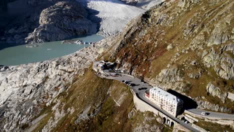 Aerial-flyover-over-Furka-mountain-pass-at-the-border-of-Valais-and-Uri-in-Switzerland,-a-popular-road-trip-destination-thanks-to-its-alpine-glacier-views