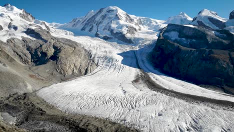 Aerial-flyover-towards-Gorner-glacier-in-Zermatt,-Switzerland-with-a-pan-down-view-from-Dufourspitze-and-Monte-Rosa-down-to-the-frozen-crevasses-on-a-sunny-summer-day