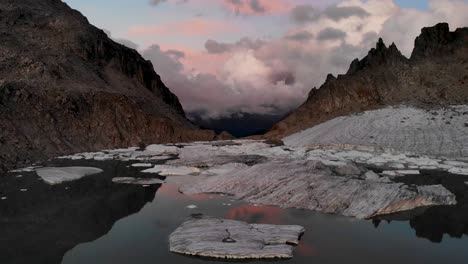 Spinning-aerial-flyover-above-a-glacier-lake-full-of-melted-icebergs-in-remote-parts-of-the-Swiss-Alps-during-sunset-with-a-pan-down-from-the-horizon-reflection-to-overhead-of-the-ice-chunks