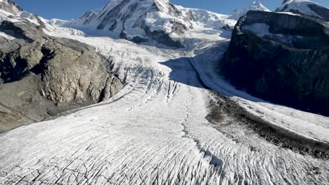 Aerial-flyover-over-Gorner-glacier-in-Zermatt,-Switzerland-with-a-pan-down-view-from-Dufourspitze-and-Monte-Rosa-down-to-the-frozen-crevasses-on-a-sunny-summer-day