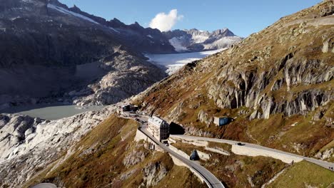 Aerial-flyover-over-Furka-mountain-pass-at-the-border-of-Valais-and-Uri-in-Switzerland-with-a-view-of-the-road,-glacier-and-hotel