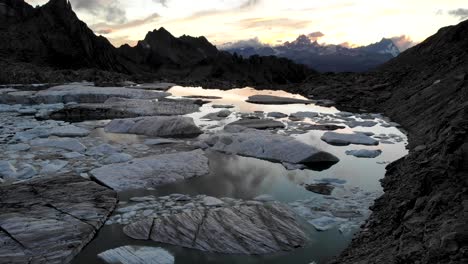 Luftaufnahme-Von-Eisbergen-Im-Schmelzenden-Gletschersee-In-Abgelegenen-Teilen-Der-Schweizer-Alpen-Mit-Sonnenuntergang-Im-Wasser
