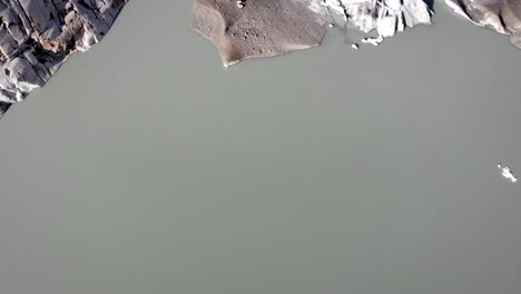 Aerial-view-of-Rhone-glacier-near-Furka-mountain-pass-at-the-border-of-Valais-and-Uri-in-Switzerland-with-a-pan-up-from-the-icebergs-in-the-glacial-lake-up-to-the-mountain-peaks