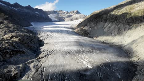 Aerial-flyover-over-Rhone-glacier-near-Furka-mountain-pass-at-the-border-of-Valais-and-Uri-in-Switzerland-with-a-pan-down-from-the-ice-to-glacial-lake