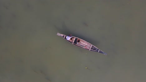 Aerial-Birds-Eye-View-Of-Lone-Fisherman-On-Traditional-Wooden-Boat-Floating-On-The-Ichamati-River