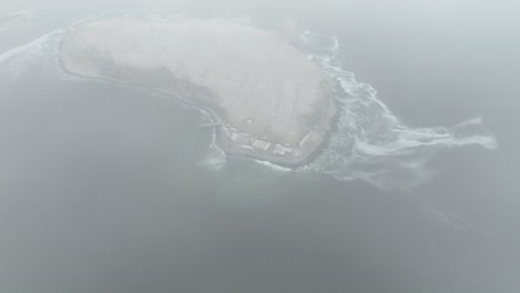 Aerial-descending-drone-shot-over-the-clouds-revealing-an-uninhabited-island-isla-san-pedro-in-the-pacific-ocean-in-the-gulf-of-california-overlooking-the-coast-with-high-waves-in-the-sea