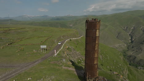 Car-Driving-On-The-Road-At-Mtkavari-Valley-With-Old-Rusted-Water-Tower-Near-Apnia,-Georgia