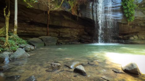 Eine-Abgelegene-Lagune-Und-Ein-Wasserfall-Fließen-über-Eine-Höhlenunterkunft-In-Tropischer-Umgebung