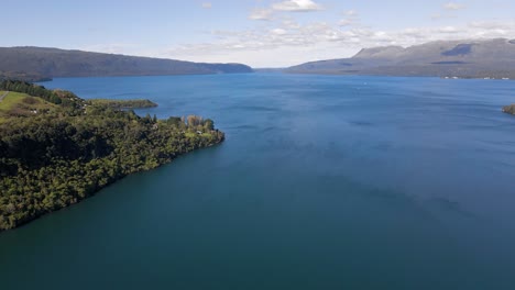 Aerial-panning-shot-of-Mount-Tarawera-behind-a-deep-blue-lake-bathed-in-sunshine