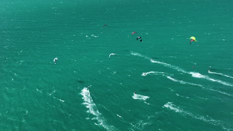 High-angle-drone---group-of-kitesurfers-flying-over-ocean-surface