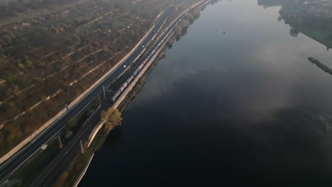 Train-driving-on-railway-along-Elbe-river-and-road-near-Melnik-city-in-Czech-Republic,-drone-following-evening-view
