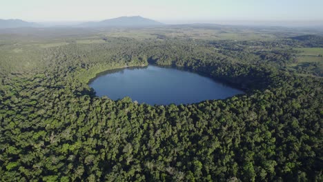 Tranquilo-Lago-De-Cráter-Rodeado-De-Exuberante-Selva-Tropical---Lago-Eacham-En-Atherton-Tableland,-Queensland,-Australia---Toma-Aérea