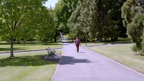 Unidentified-man-walking-on-road-in-the-middle-of-the-city-park-with-shady-trees