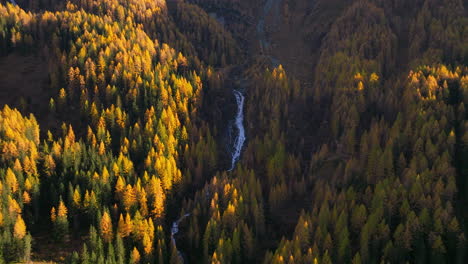 Aerial-view-orbiting-waterfall-cascading-through-Ahrntal-Casere-pristine-Autumn-woodland-valley,-South-Tyrol