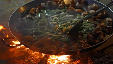 On-the-road,-close-up-on-fire-place-with-typical-pan-called-"paellero"-while-cooking-the-classic-Paella-Valenciana,-with-chicken,-green-and-white-beans