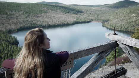 Female-Traveler-Admiring-Beautiful-Scenery-Of-Calm-Lake-And-Dense-Forest-From-Wooden-Viewing-Platform-In-Saint-Come,-Quebec,-Canada