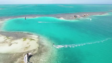 Two-Men-Kitesurf-In-Caribbean-Sea,-Palafito-Los-Roques,-Aerial-Track-View