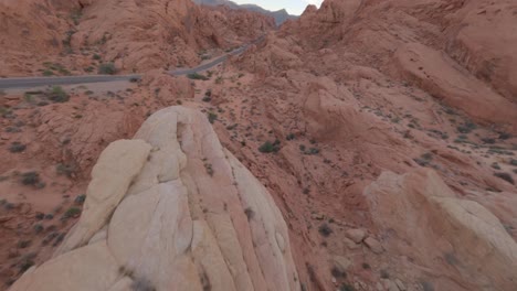 FPV-Diving-down-rocky-mountain-face-along-road,-Valley-of-Fire-,-Nevada