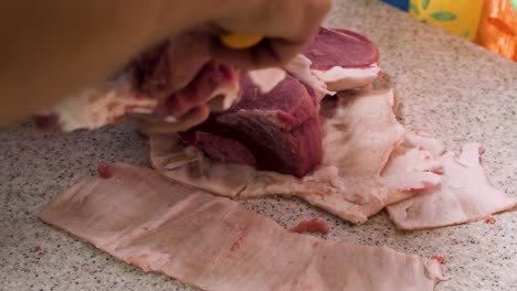 Removing-skin-from-fresh-pork-meat-pieces-in-domestic-kitchen,-close-up-view