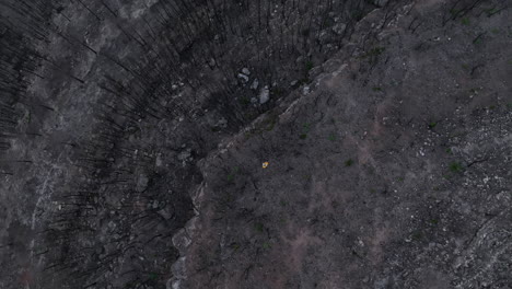 Aerial-view-flying-over-man-walking-through-burned-remains-of-forest-natural-disaster