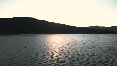 side-pan-of-sun-disappearing-behind-mountains,-vail-lake-Temecula