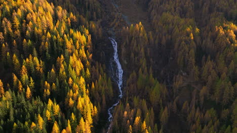 Aerial-view-orbiting-pristine-waterfall-cascading-through-Ahrntal-Casere-Autumn-woodland-valley,-South-Tyrol