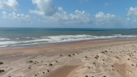 Absteigende-Drohnenbilder-Zu-Einem-Wunderschönen-Großen-Strand-Mit-Hellbraunem-Sand-An-Einem-Ruhigen-Ozean