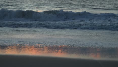 Close-up-footage-of-the-sea-rolling-in,-gently-lit-up-by-a-warm-orange-sunset,-captured-in-60fps,-slow-motion
