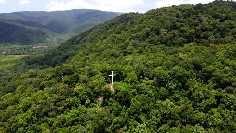 Orbit-Shot-Of-White-Cross-Deep-In-Green-Mountain-Landscape,-Ermita-Hill,-Baler,-Philippines