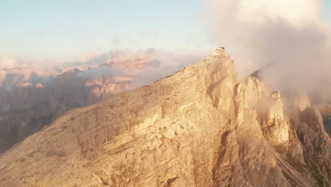 Schroffe-Seiten-Des-Mount-Nuvolau,-Beleuchtet-Von-Goldenem-Sonnenuntergang,-Nuvolau-Klippenhütte-Auf-Dem-Gipfel-Mit-Umgebenden-Wolken,-Luftaufnahme