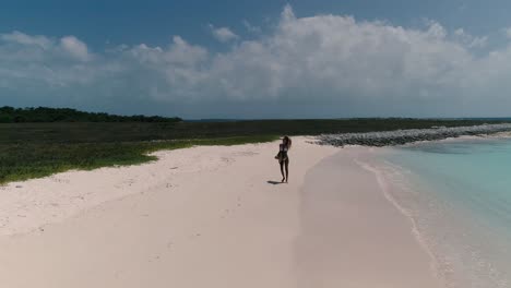 YOUNG-WOMAN-walk-on-white-sand-BEACH-WEAR-BIKINI,-WIND-MOVE-HAIR,-DRONE-LOW-FLY