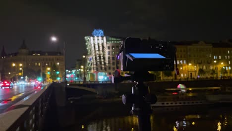 Camera-on-tripod-making-night-time-lapse-of-Prague-traffic,-Dancing-House-blurry-lights-background