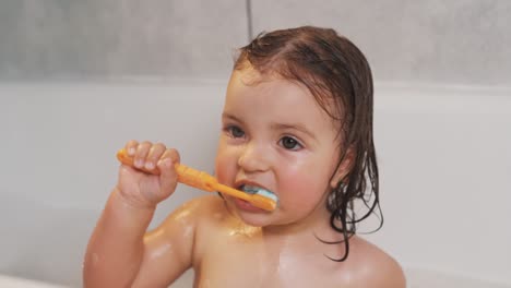 Close-up-portrait-of-a-cute-two-year-old-girl-brushing-her-teeth-while-sitting-in-the-bathroom