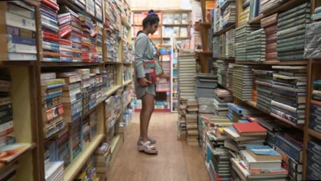 Asian-girl-walking-between-the-rows-of-bookshelves,-Side-angle-shot
