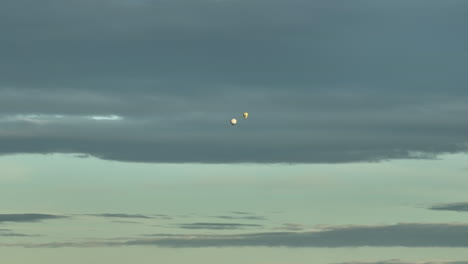 Distant-View-Of-Two-Hot-Air-Balloons-Flying-Against-Cloudy-Sky-At-Sunset