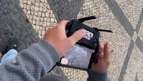 Male-hand-flying-drone-against-portuguese-cobblestones-background-at-Praca-Camoes